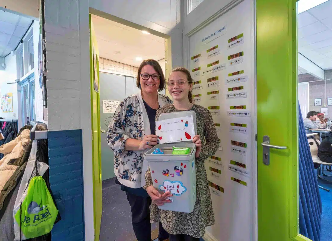 Een scholier en docent staan met de gratis menstruatieproducten op een school.